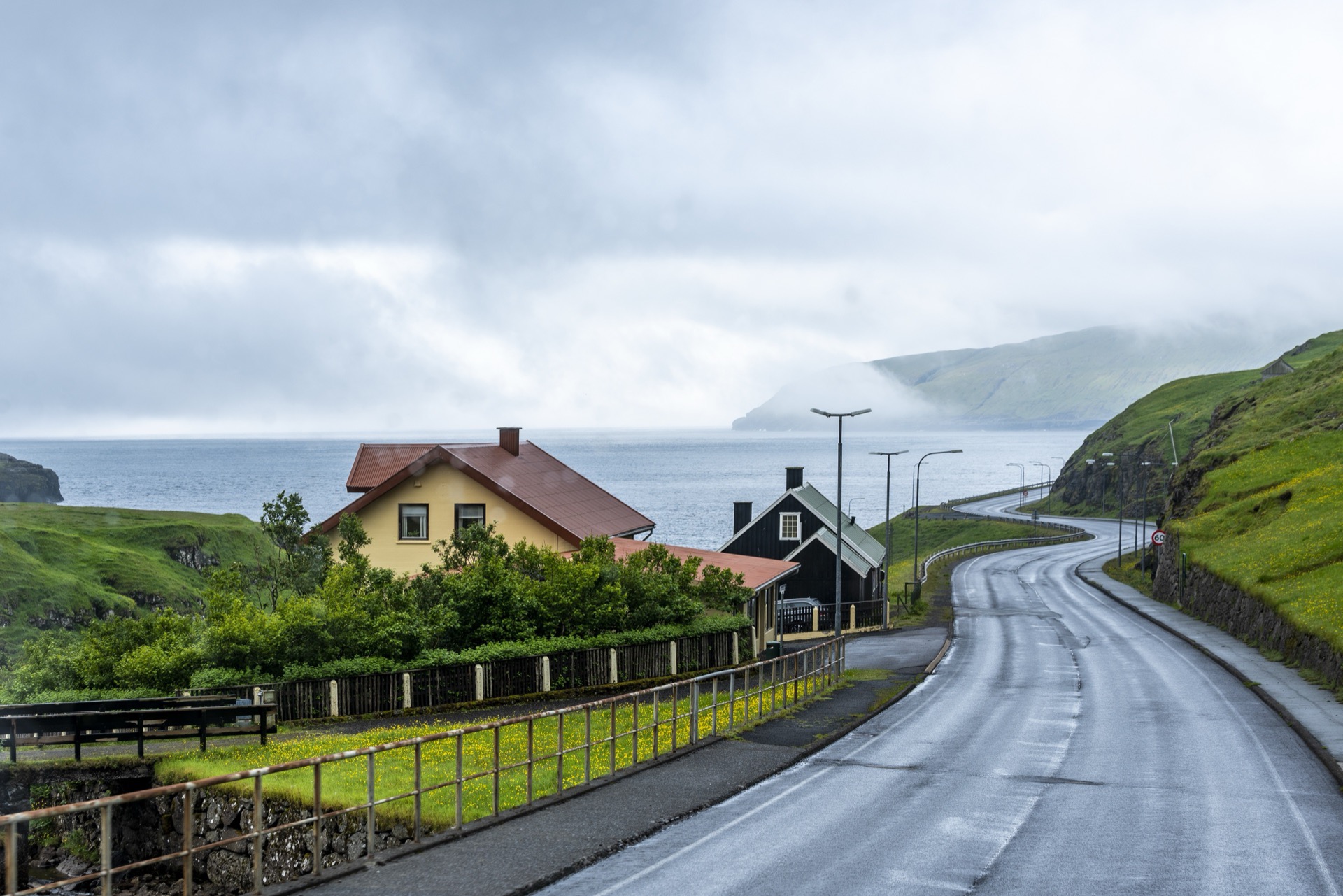Krokig kustväg förbi ett gult hus en dimmig dag vid havet